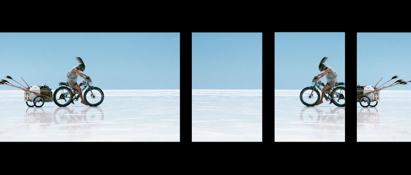 Film still from John Harvey's Canopy featuring a traveler on motor bike across salt plains